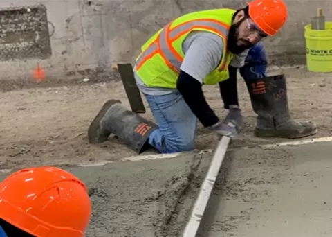 person wearing a reflective vest and hardhat measuring a section of oncrete