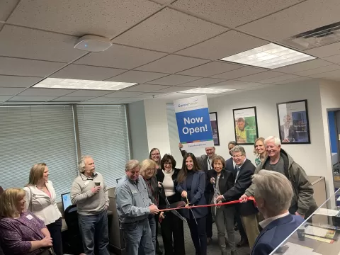a crowd of people standing in a room with a ribbon and scissors