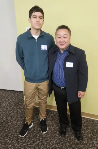 two individuals standing together in front of a yellow wall
