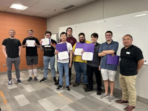 photo of a large group of people standing in a room, some holding certificates