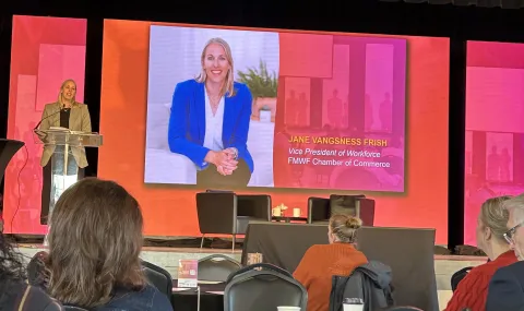 photo of person speaking at the front of a room with an orange backdrop